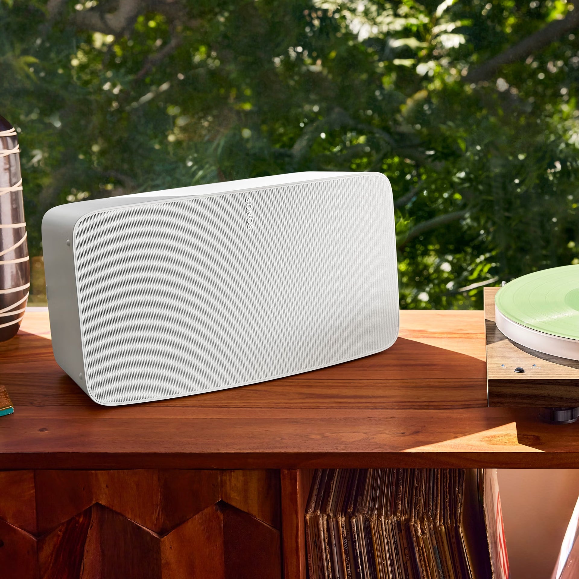 White Sonos speaker on a wooden surface with greenery in the background
