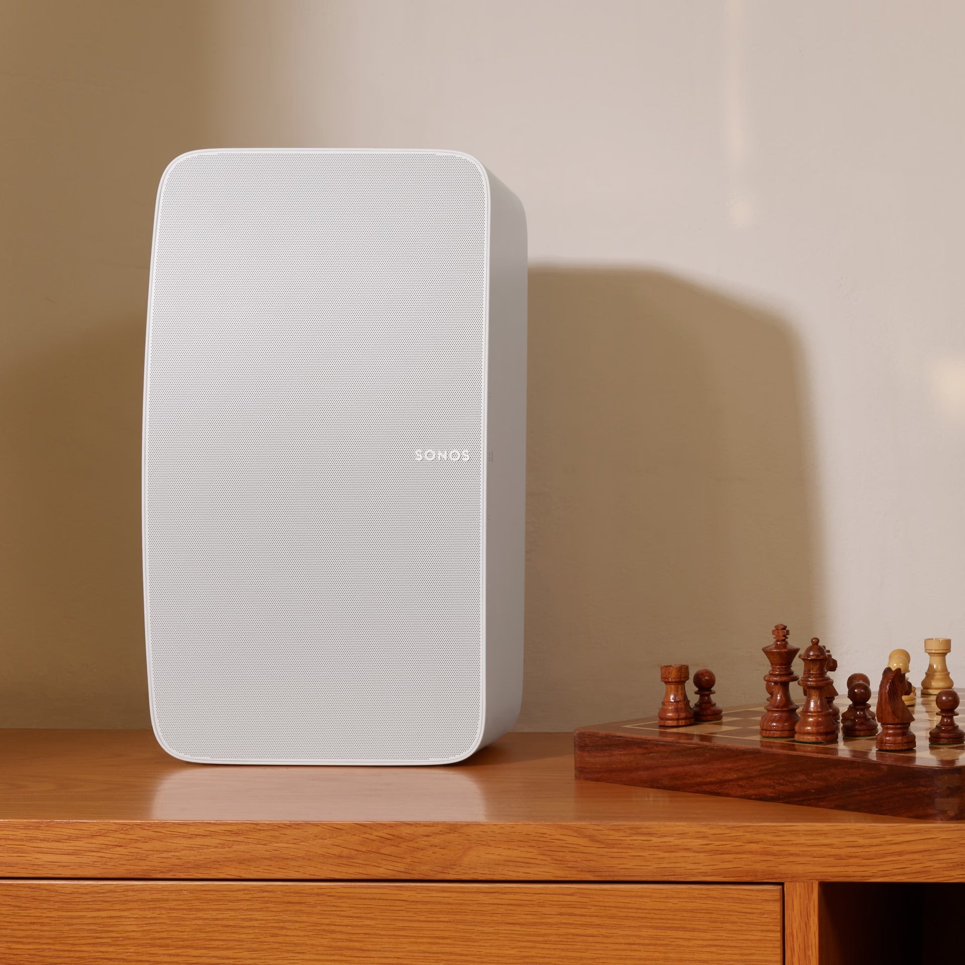 White Sonos speaker on a wooden surface with chess pieces in the background