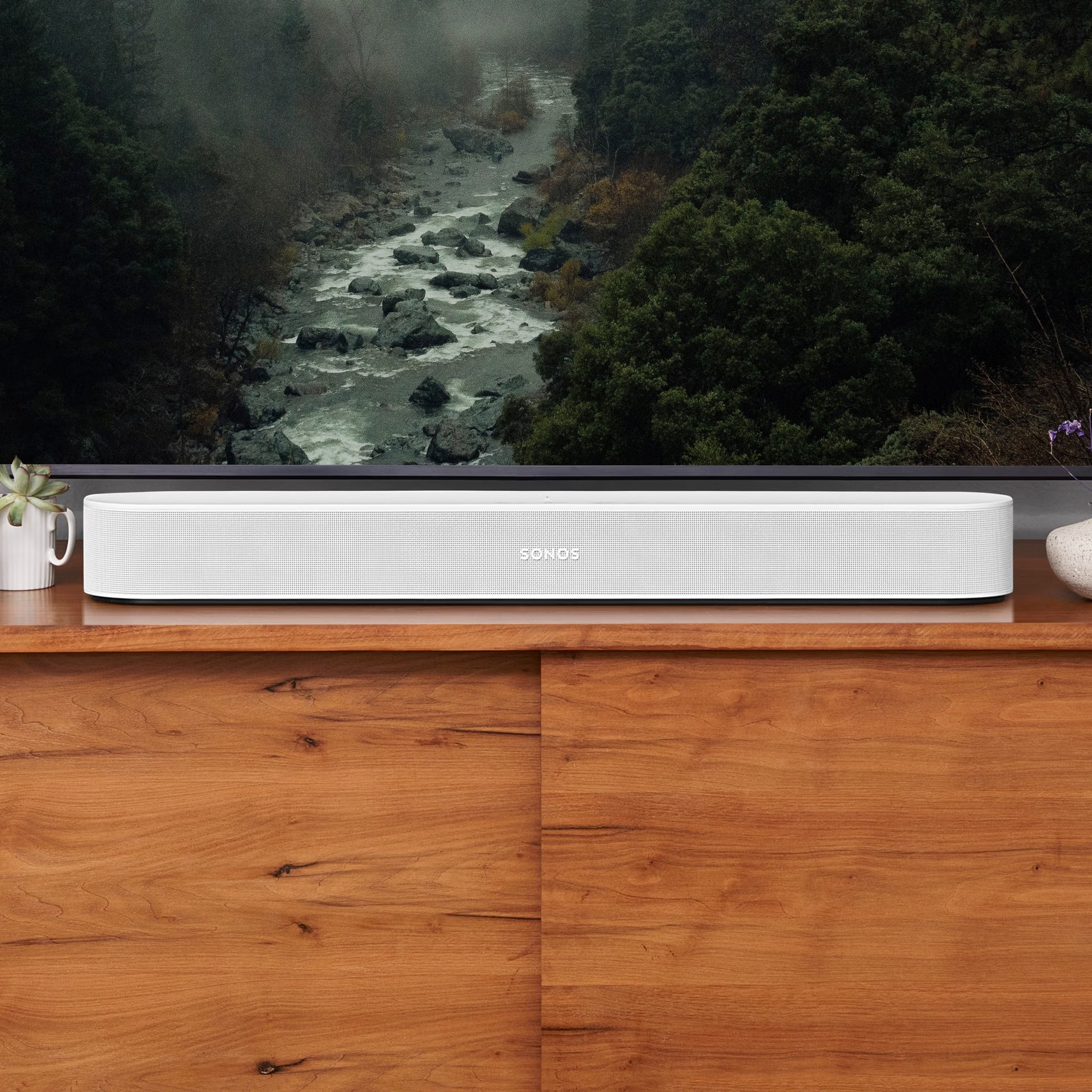 Sonos Beam Gen 2 white below wall-mounted TV in bright modern living room — compact Dolby Atmos soundbar