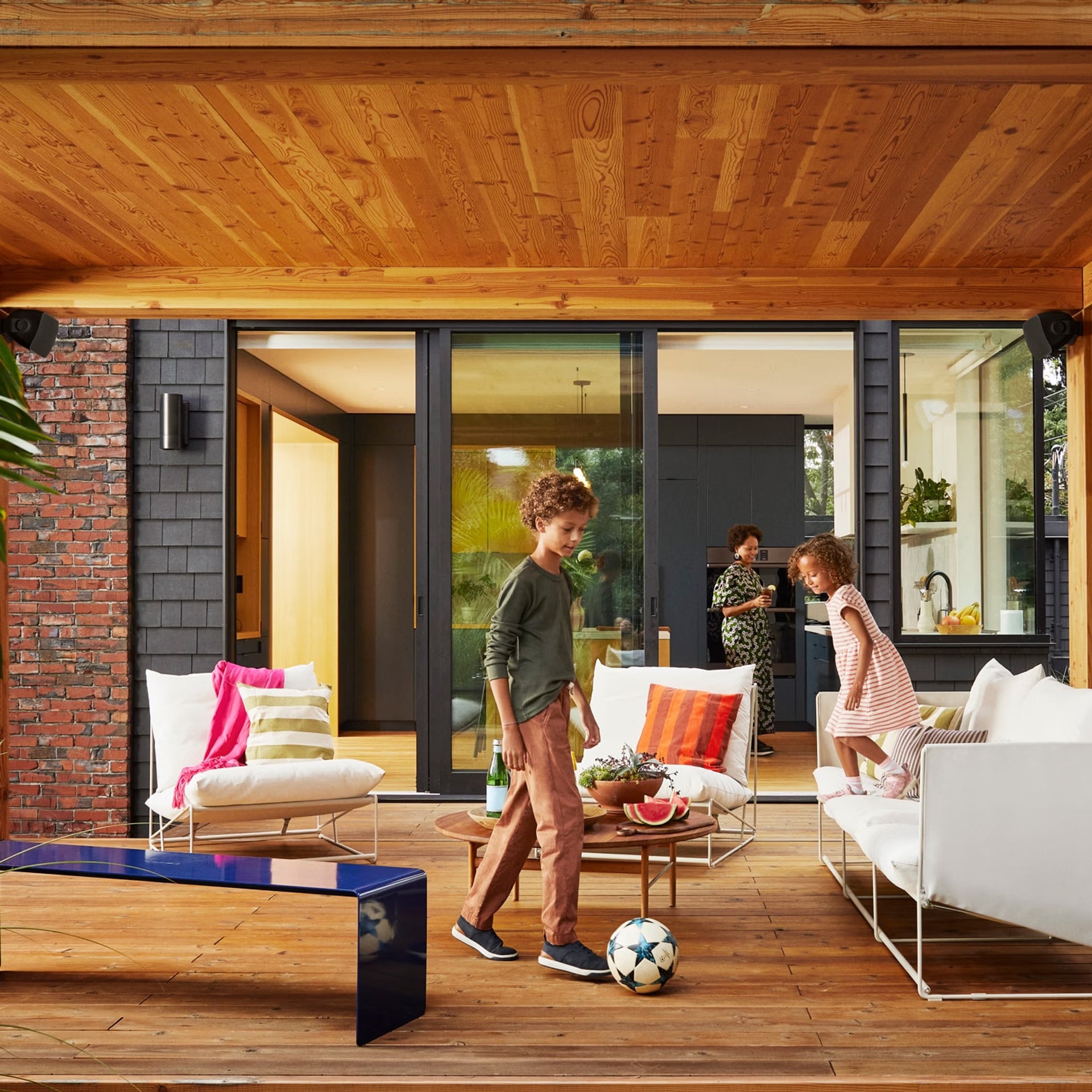 Children playing with a soccer ball on a wooden deck of a modern house.Family entertaining outdoors with Sonos Outdoor by Sonance black — HiFi weatherproof stereo garden audio