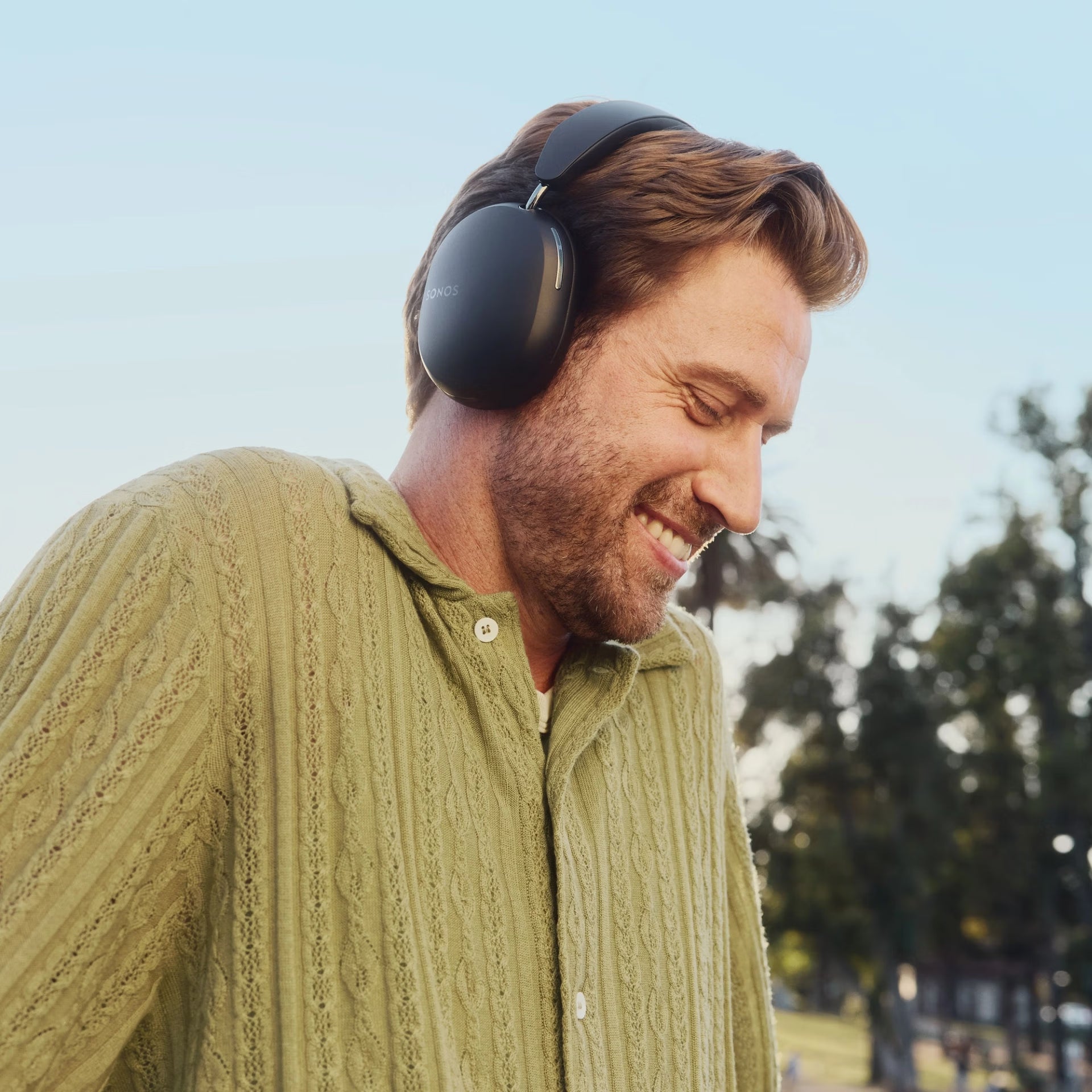 Man wearing SonosAce_Black headphones outdoors with trees and clear sky in the background